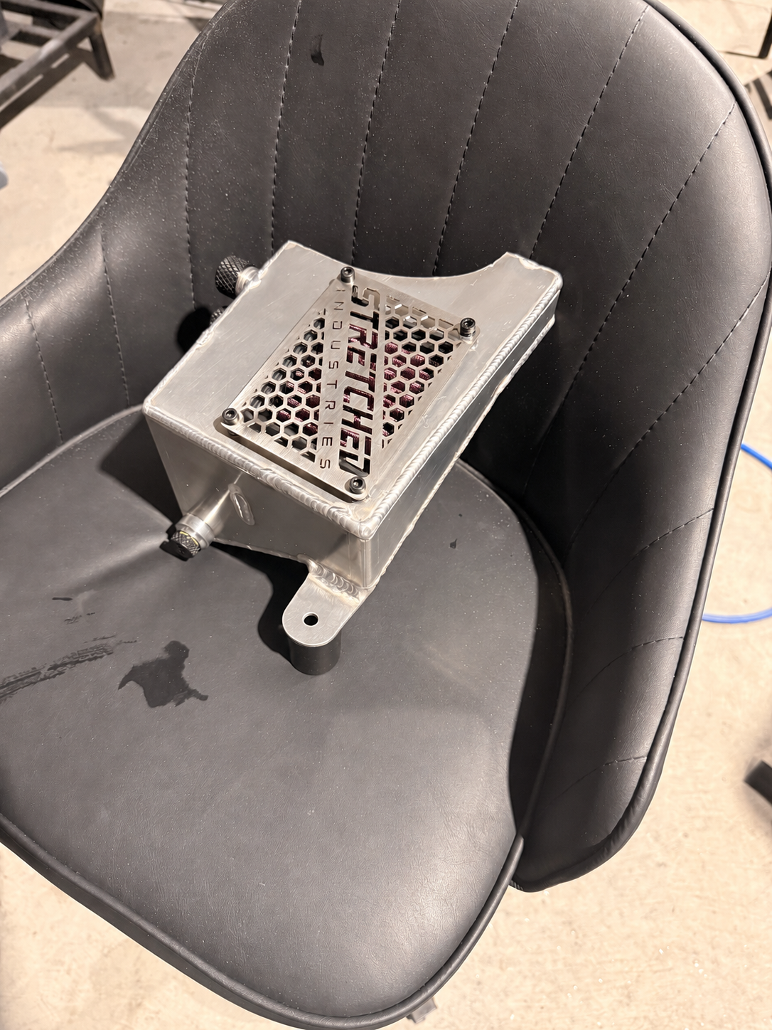 Overhead view of the aluminium standalone catch-can prototype and branded vent cover, photo edited to show the original short mounting leg